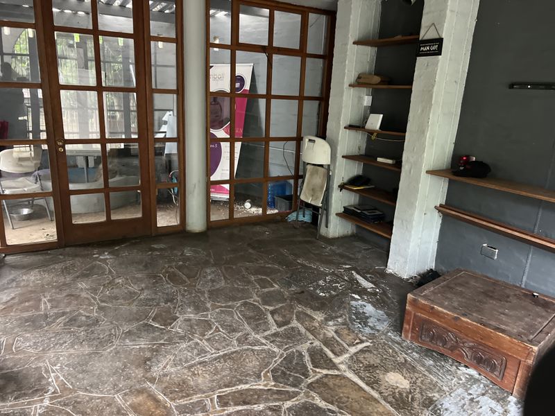 A rustic indoor space featuring stone flooring, built-in wooden shelving, and large timber-framed glass doors leading to an outdoor area.