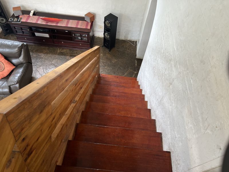 A view looking down a wooden staircase with a timber balustrade, leading into a living area with stone flooring.