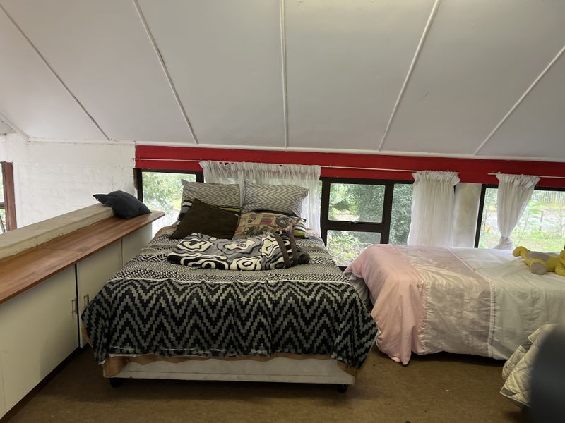 A bedroom located in an attic space featuring a sloped ceiling, built-in cabinetry, and large windows overlooking the garden.