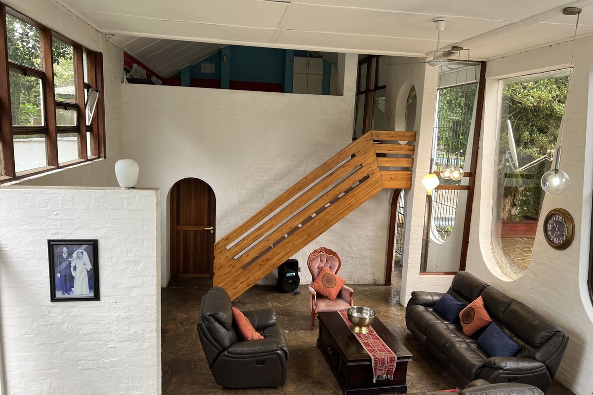 Spacious living area featuring a unique wooden staircase, high ceilings, and large windows that provide ample natural light and garden views.