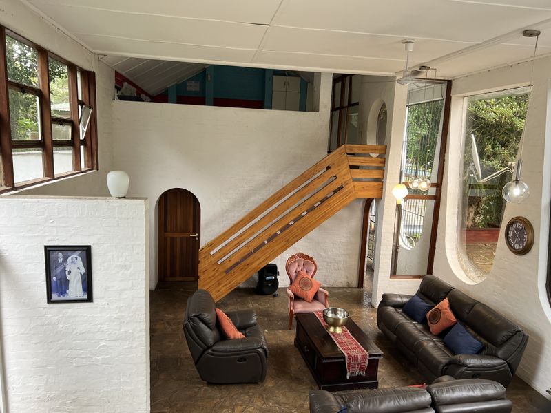 Spacious living area featuring a unique wooden staircase, high ceilings, and large windows that provide ample natural light and garden views.