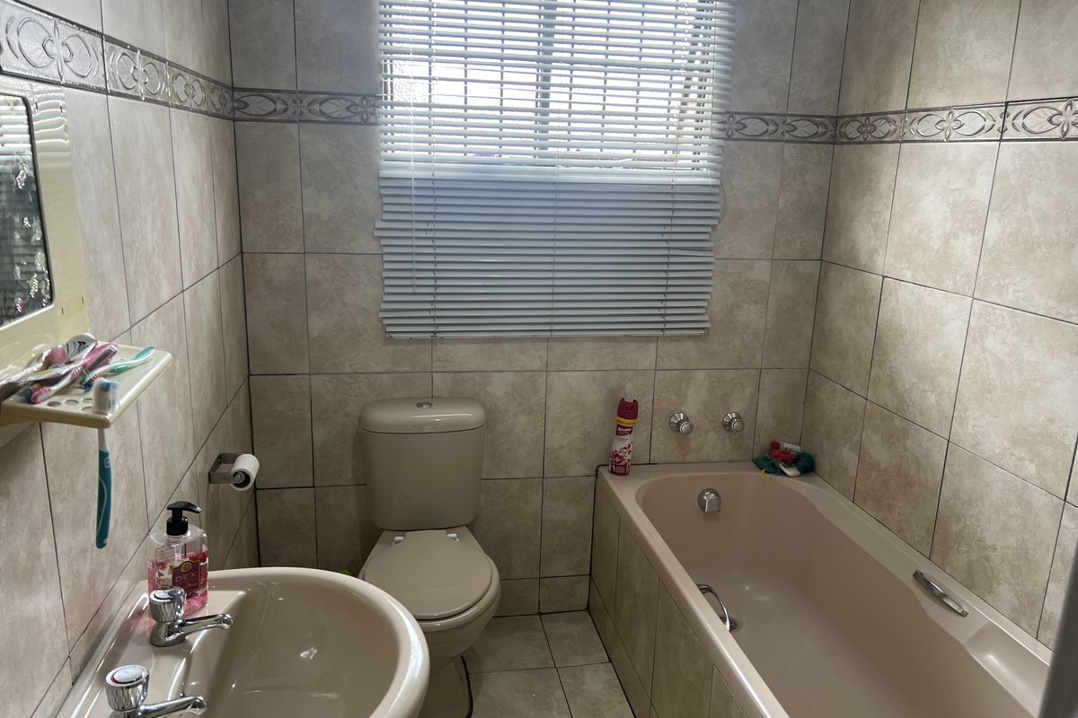 A functional bathroom featuring a bathtub, toilet, and pedestal sink with full-height wall tiling and a window with fitted blinds.