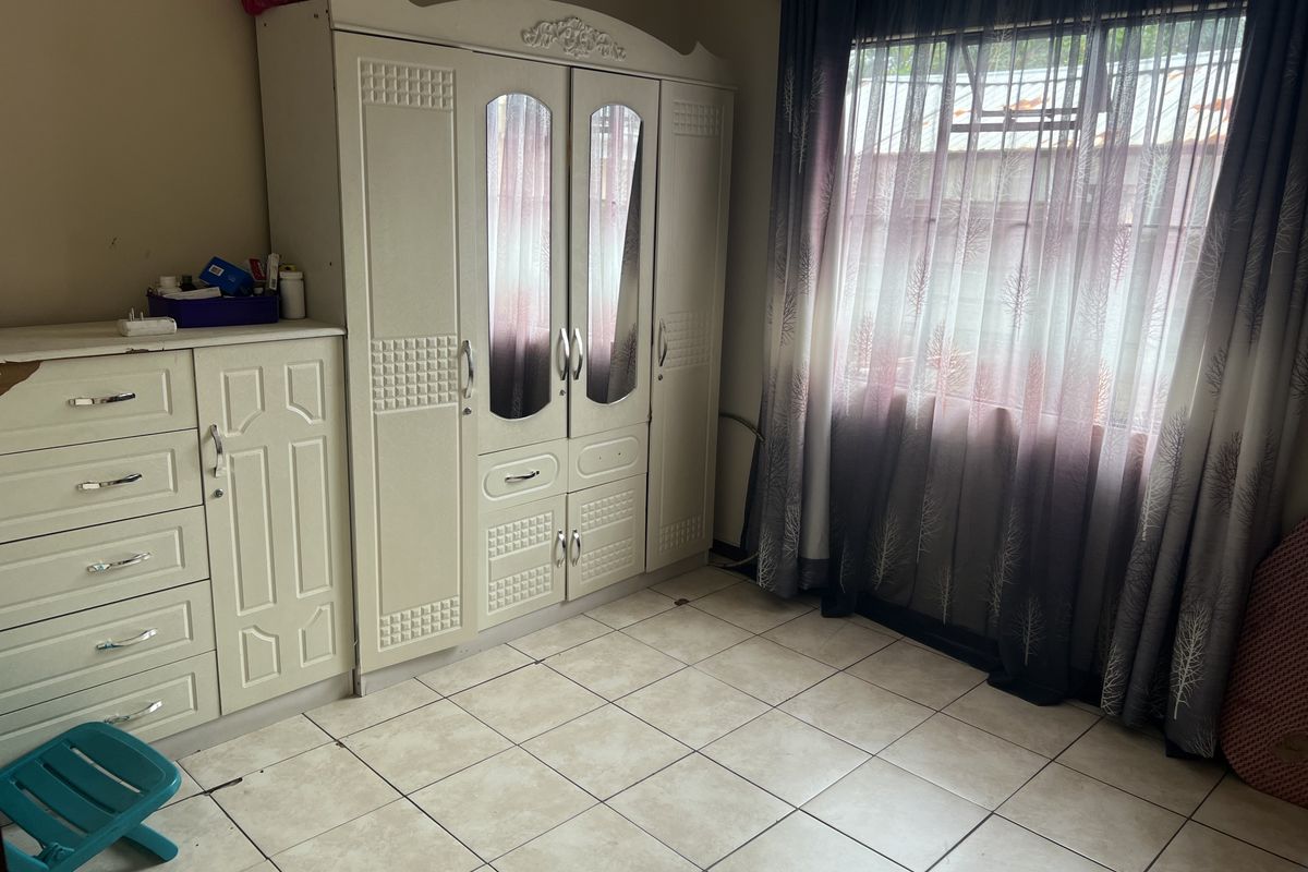 A bedroom featuring tiled flooring and a window with curtain treatments.