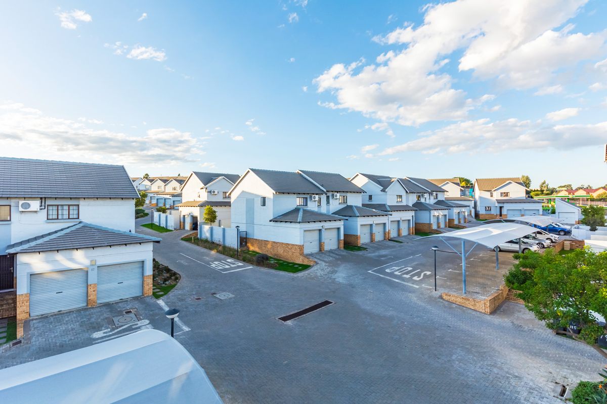 An elevated view of a residential apartment complex featuring paved driveways, multiple garage units, and covered parking bays under a clear blue sky.