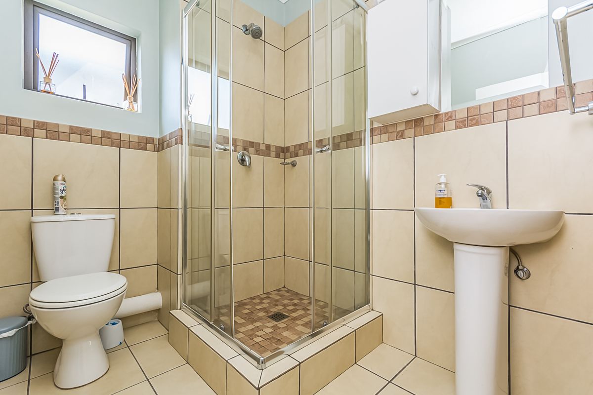 A functional bathroom featuring a glass-enclosed shower, pedestal basin, and toilet with neutral wall and floor tiling.
