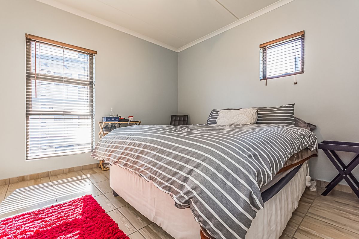A well-lit bedroom featuring tiled flooring, two windows with fitted blinds, and neutral wall finishes.