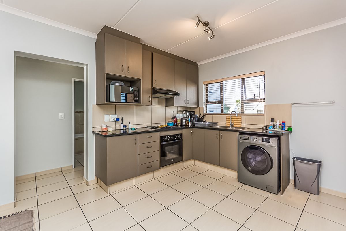 Functional kitchen featuring dark cabinetry, tiled flooring, built-in oven, hob, extractor fan, and space for a washing machine.
