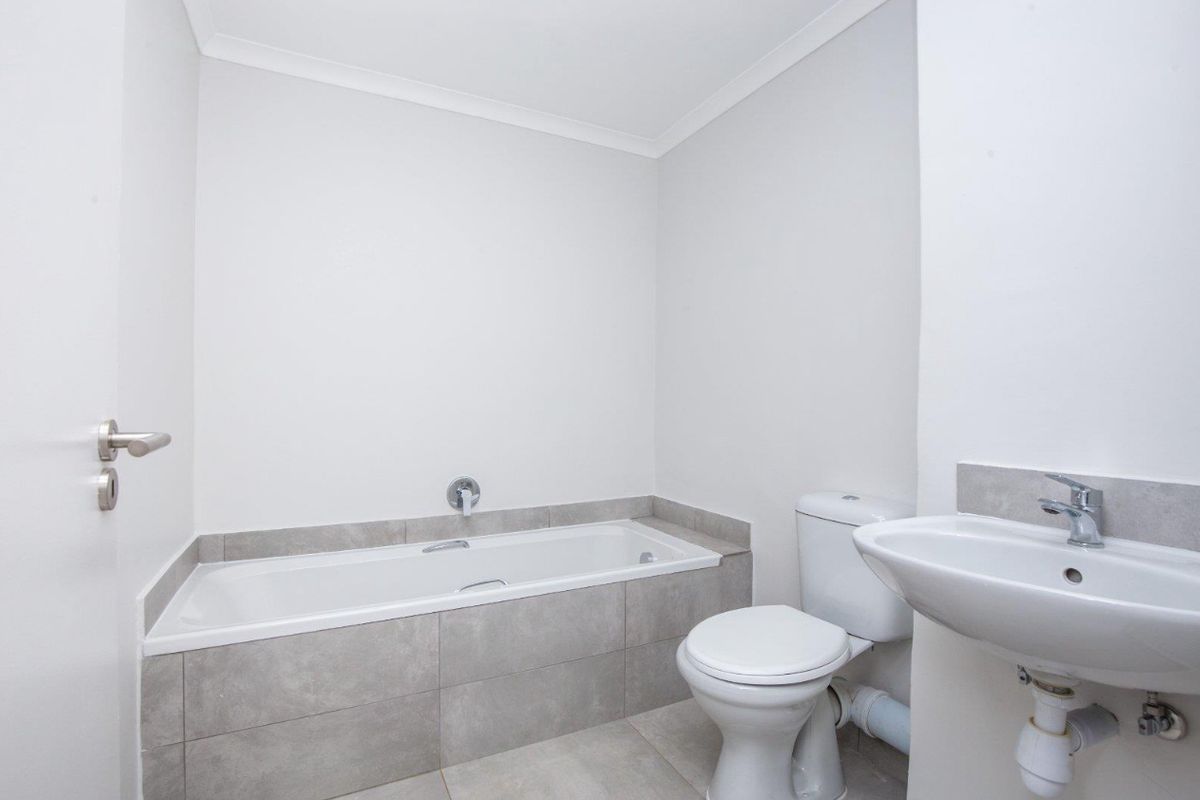A clean, modern bathroom featuring a built-in bathtub with grey tiling, a white ceramic toilet, and a wall-mounted basin.