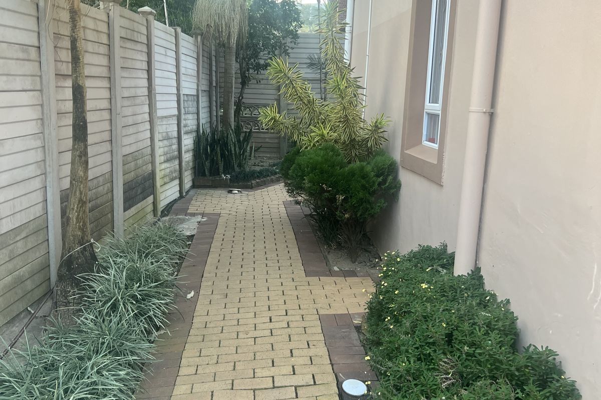 A paved side walkway featuring established garden beds and a concrete boundary wall along the side of the townhouse.