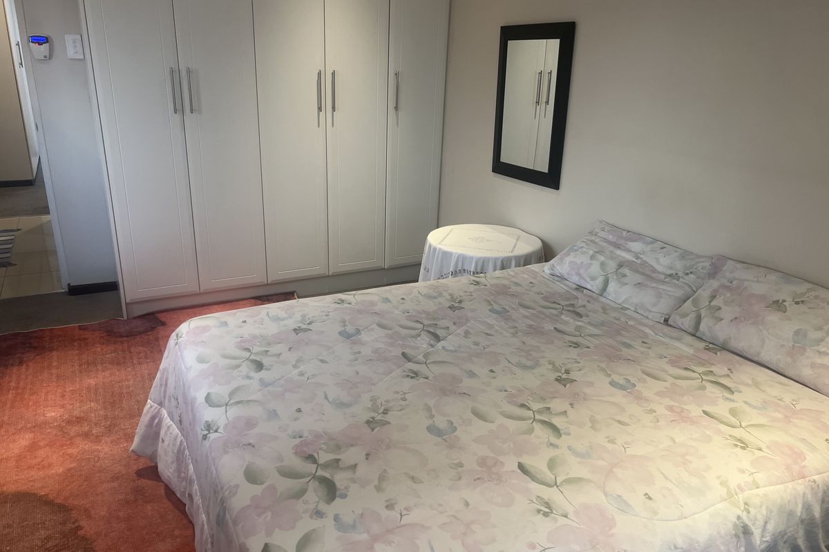A well-maintained bedroom featuring built-in floor-to-ceiling wardrobes with modern handles and neutral wall finishes.