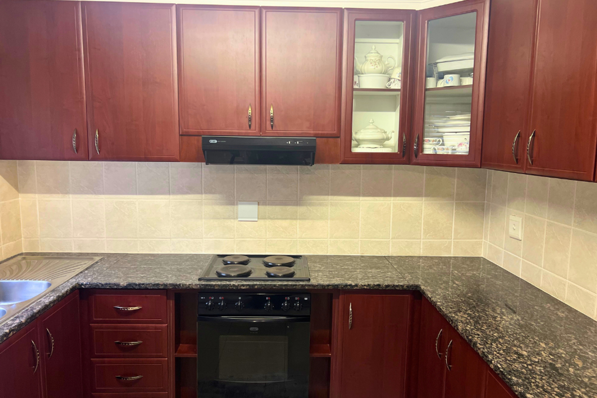 A functional kitchen featuring dark wood cabinetry, granite countertops, a built-in oven, electric hob, extractor fan, and tiled backsplash.