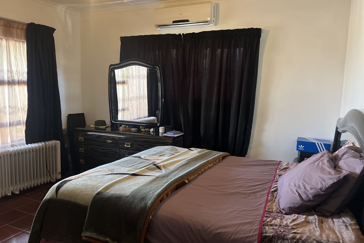 A bedroom featuring a wall-mounted air conditioning unit, tiled flooring, and a ceiling fan.