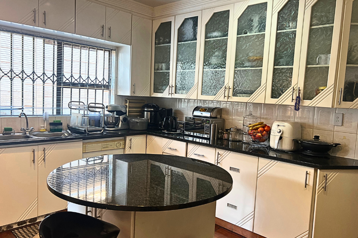 A functional kitchen featuring cream-colored cabinetry with glass-paneled upper doors, dark granite countertops, and a central circular breakfast bar island.