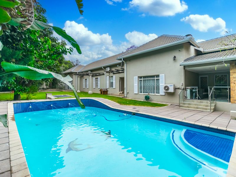 A well-maintained rear garden featuring a swimming pool with water features, a tiled patio area, and direct access to the main house structure.