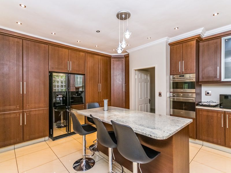Modern kitchen featuring dark wood cabinetry, granite island countertop, built-in oven and microwave, and recessed lighting with tiled flooring.