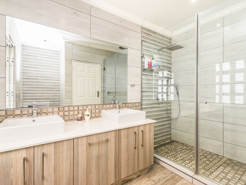 Modern bathroom featuring a double vanity with vessel sinks, a large wall-mounted mirror, and a spacious walk-in shower with a glass enclosure.