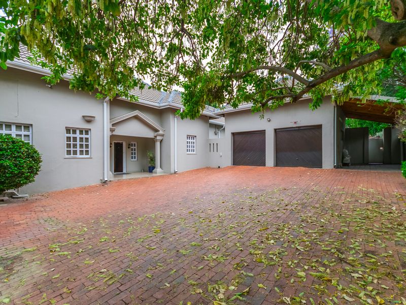 Front elevation of a house featuring a spacious brick-paved driveway, a double garage, and a covered entrance porch with classic architectural detailing.
