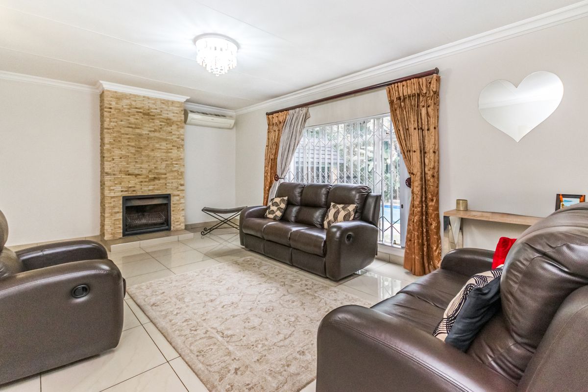 A well-maintained living room featuring a stone-clad fireplace, tiled flooring, and a split-system air conditioner, offering a comfortable and functional living space.