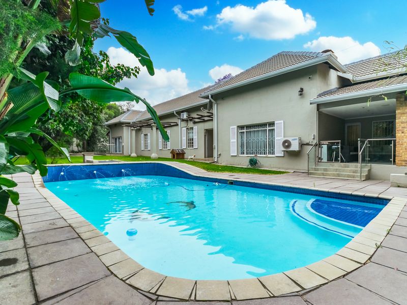 Spacious rear garden featuring a large swimming pool with integrated water features, adjacent to a covered patio area and the main house structure.
