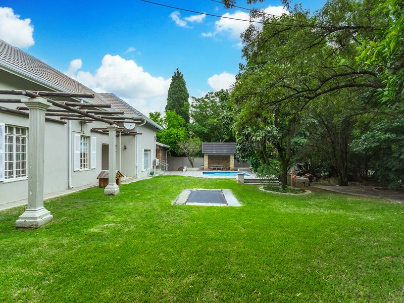 Spacious rear garden featuring a lawn, in-ground trampoline, pergola-covered patio area, and a swimming pool with a dedicated lapa.