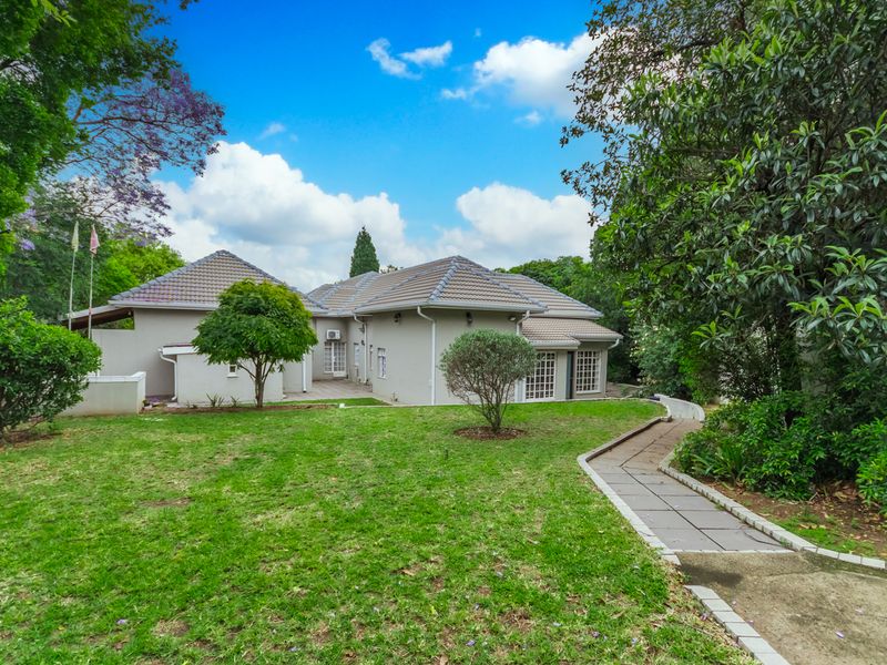 A view of the rear elevation of the house featuring a well-maintained garden, tiled roof, and a paved walkway leading to the property.