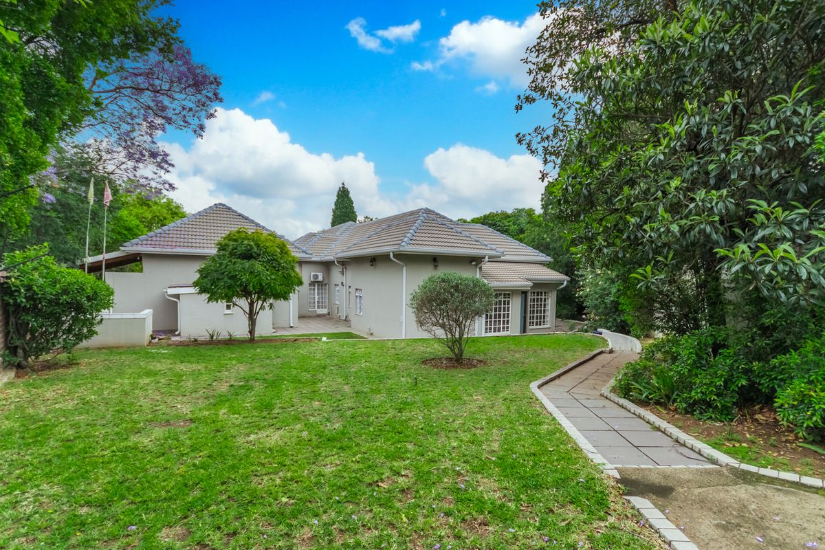 A view of the rear elevation of the house featuring a well-maintained garden, tiled roof, and a paved walkway leading to the property.