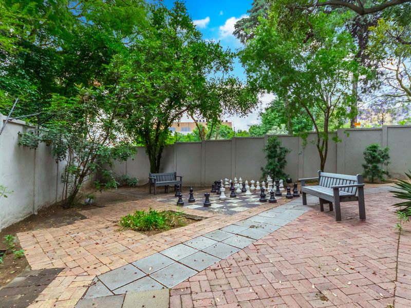 A private garden area featuring a paved patio, perimeter walling, and mature trees, providing a quiet outdoor space.