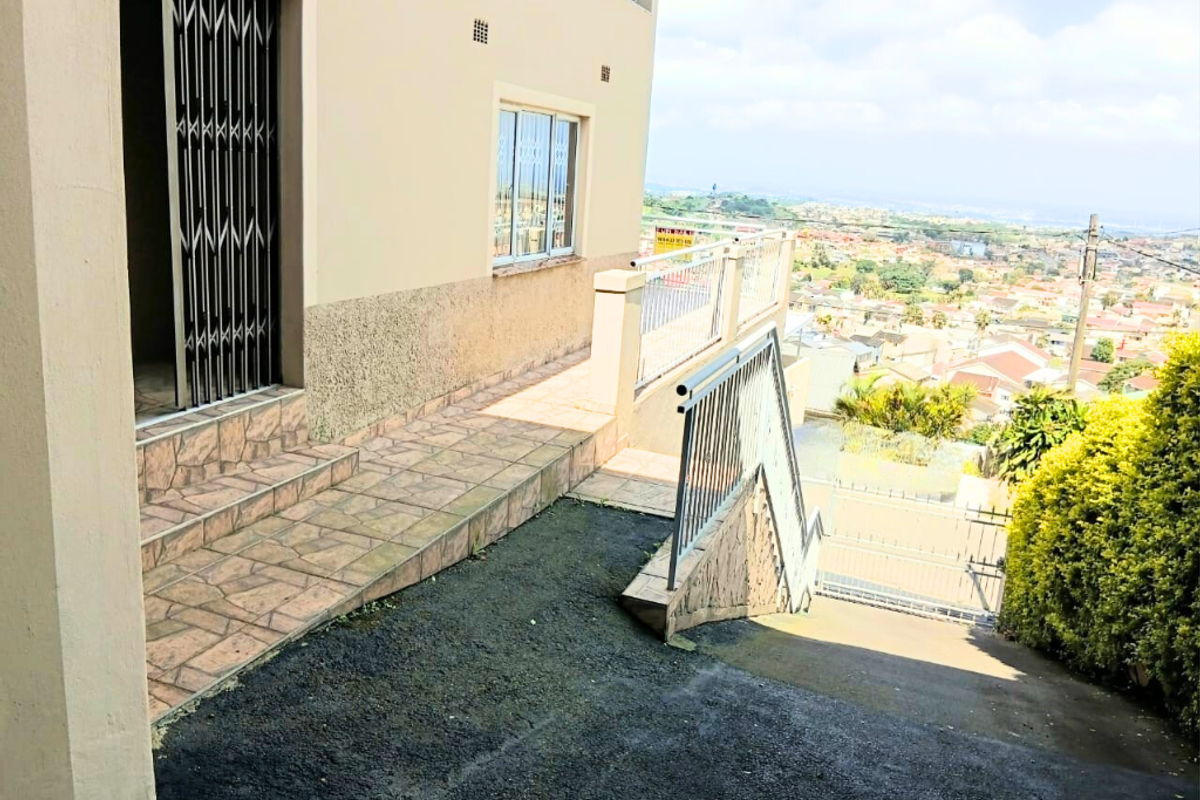 Exterior view of the property featuring a paved walkway, metal security gate, and staircase leading down to the driveway with expansive neighbourhood views.