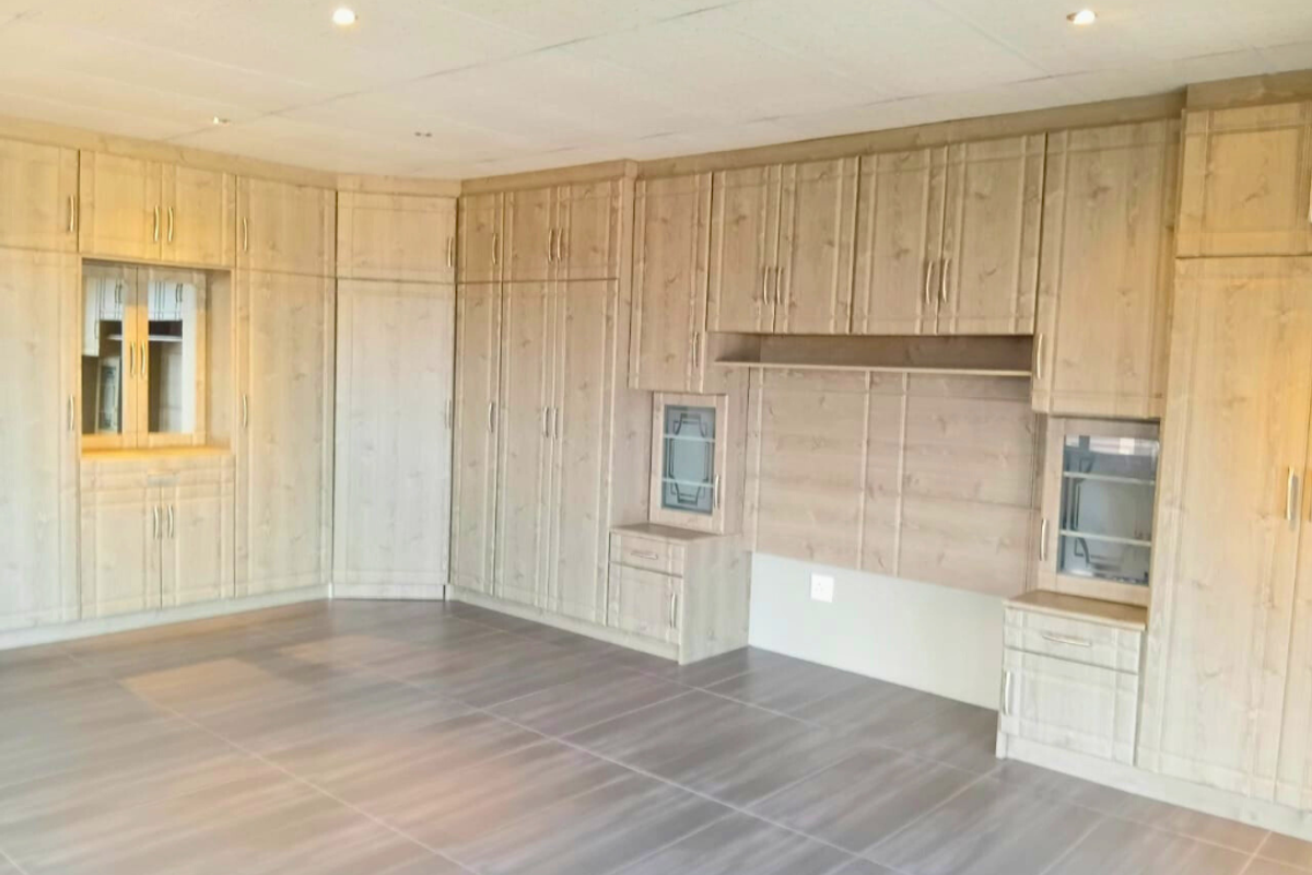 A spacious room featuring extensive built-in wooden cabinetry with integrated shelving and storage, complemented by neutral tiled flooring and recessed ceiling lighting.
