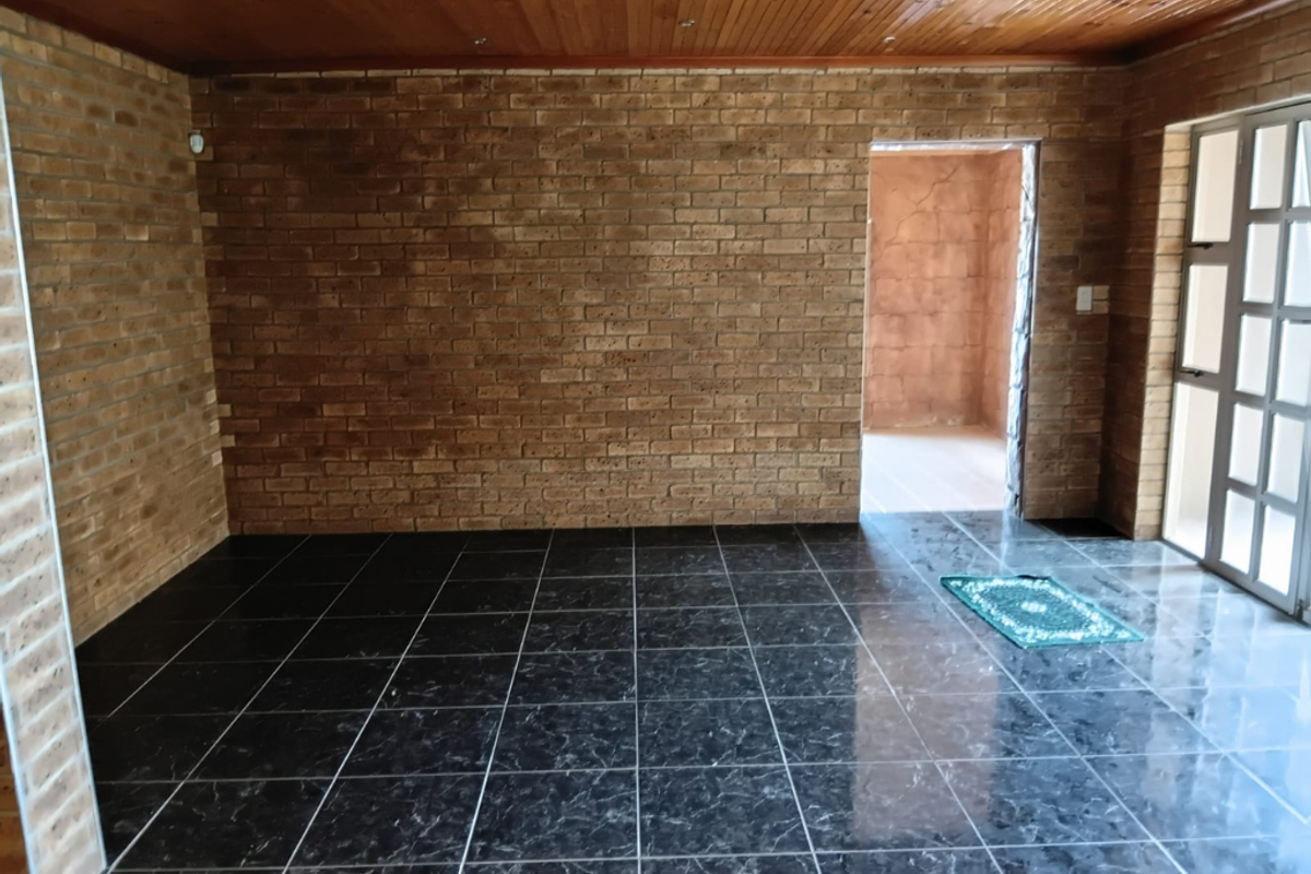 An empty living area featuring exposed brick walls, dark marble-effect floor tiles, and a timber-paneled ceiling with recessed lighting.