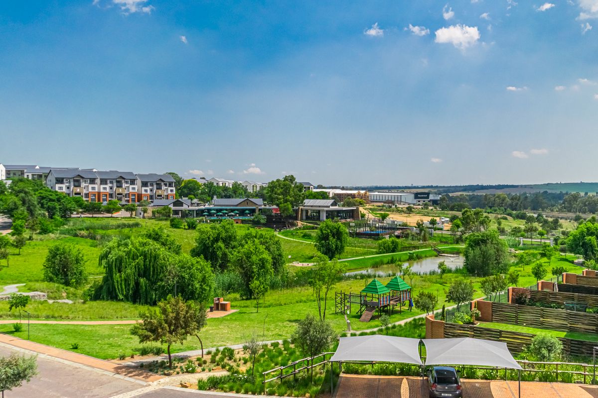 Elevated aerial view of a landscaped residential estate featuring green spaces, a small pond, playground equipment, and communal parking areas.