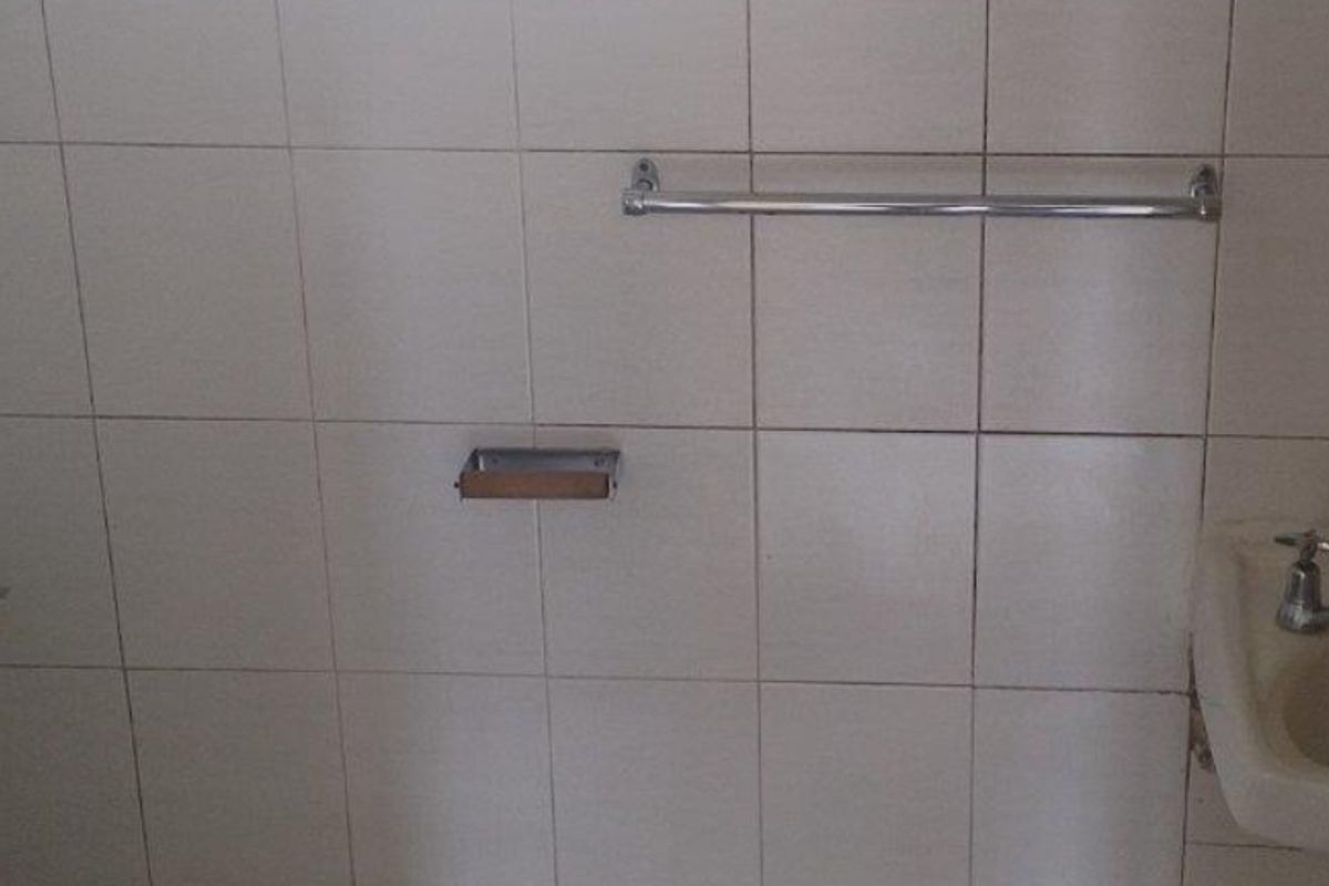 A functional bathroom featuring a standard toilet, wall-mounted basin, and tiled walls with a privacy window.