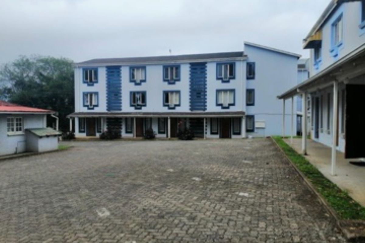 Exterior view of a multi-story residential flat complex featuring paved courtyard area and covered walkways.