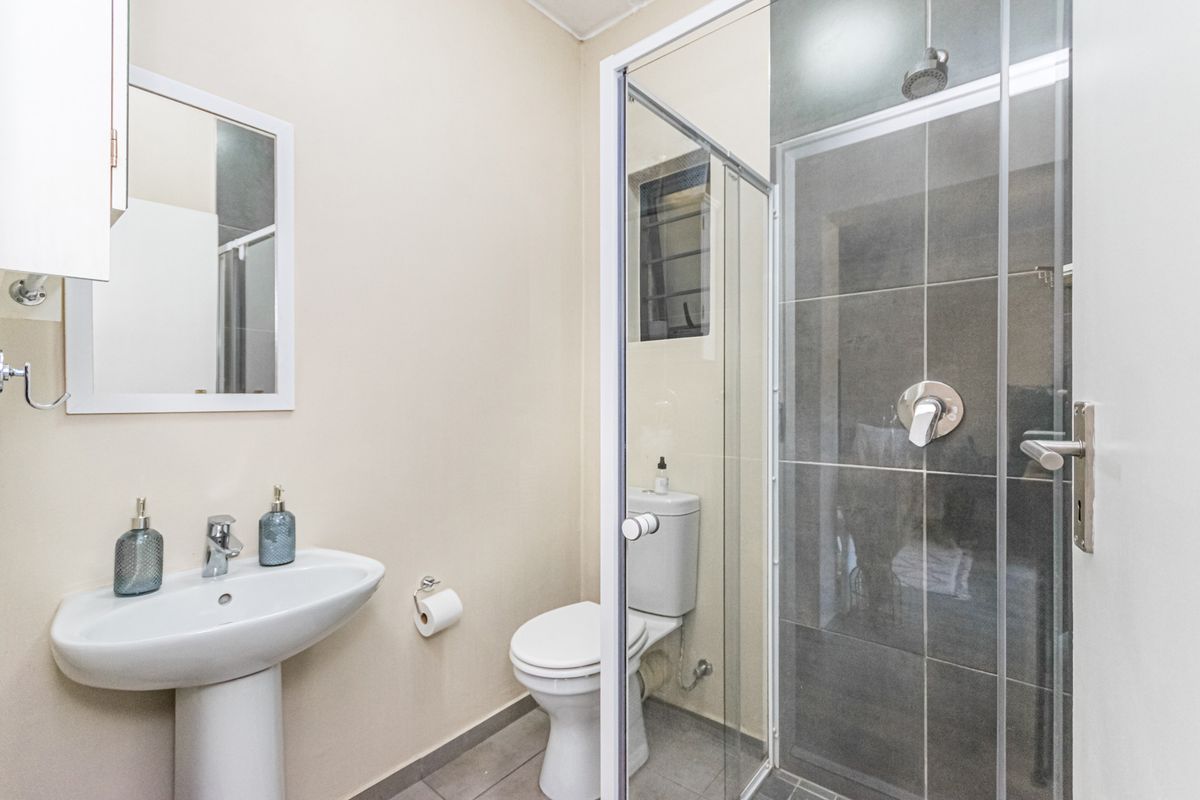 A functional bathroom featuring a pedestal basin, a toilet, and a glass-enclosed shower with dark tiled walls.