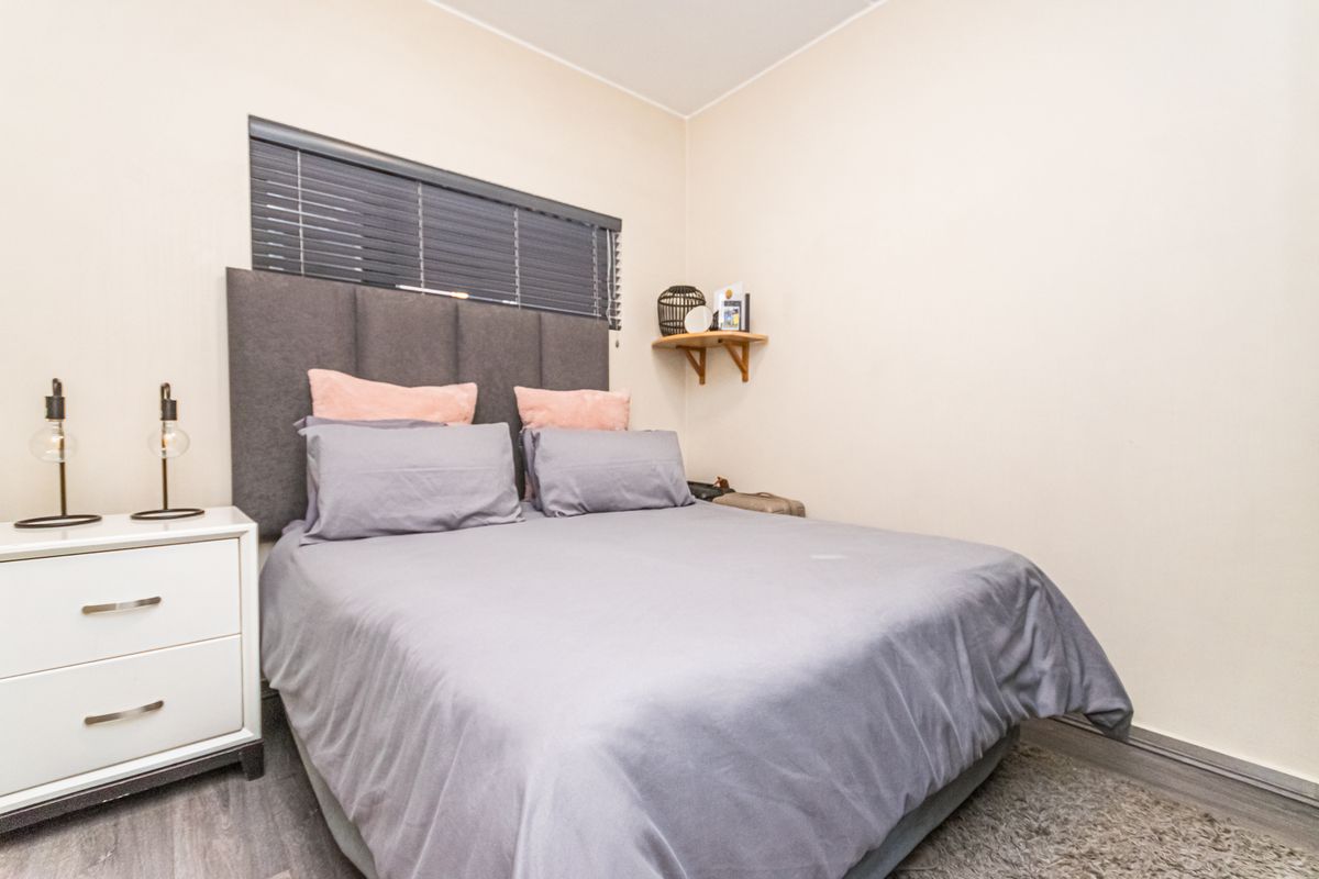 A compact bedroom featuring neutral wall finishes, grey wood-look flooring, and a horizontal window fitted with dark venetian blinds.