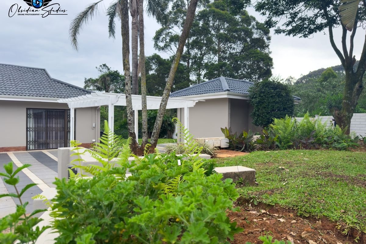 A view of the property exterior featuring a landscaped garden, paved driveway, and a white pergola structure connecting the building sections.