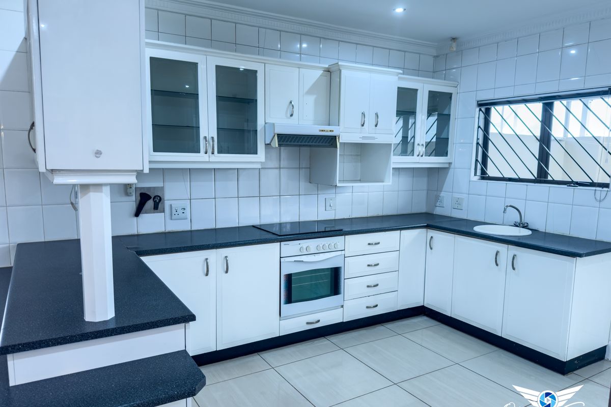 A clean, functional kitchen featuring white cabinetry, dark countertops, a built-in oven, hob, extractor fan, and tiled splashbacks.
