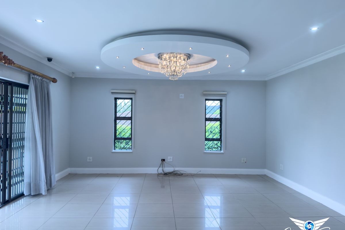 Spacious living area featuring a decorative circular recessed ceiling with integrated lighting, tiled flooring, and large windows with security bars.