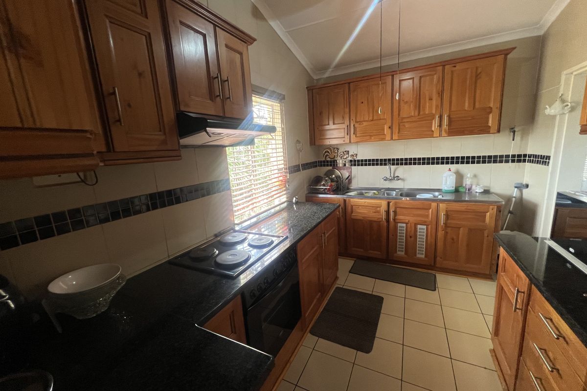 A functional kitchen featuring solid wood cabinetry, granite countertops, a built-in electric hob and oven, and tiled flooring.