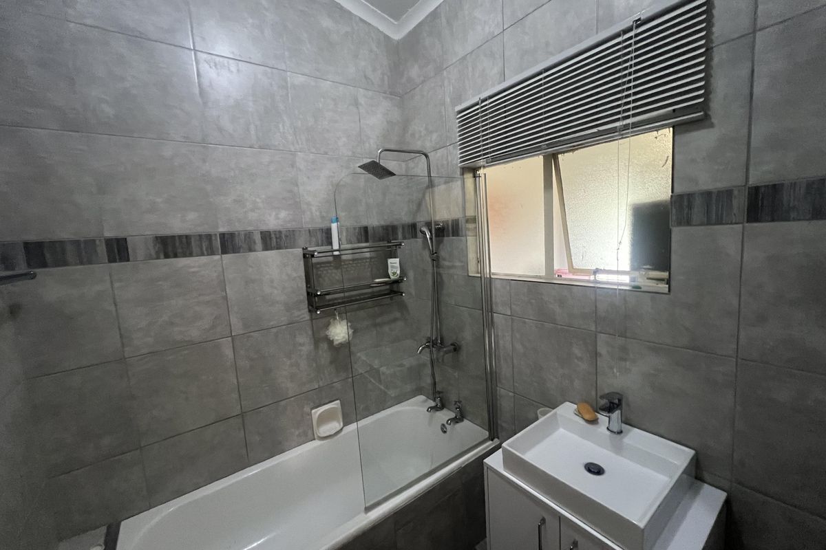 Modern bathroom featuring grey wall tiles, a built-in bathtub with a glass shower screen, rainfall showerhead, and a contemporary vanity basin.