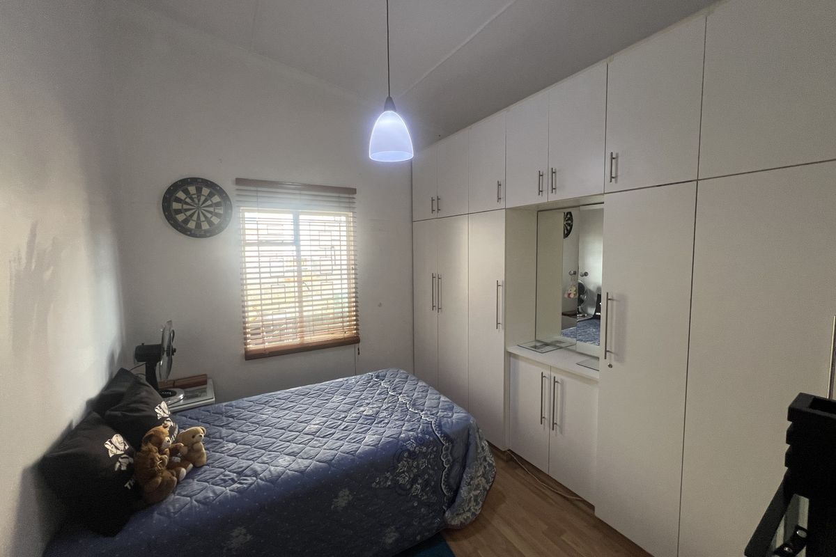 A well-maintained bedroom featuring extensive built-in floor-to-ceiling cabinetry with integrated vanity and mirror, complemented by wood-look flooring and a window with blinds.