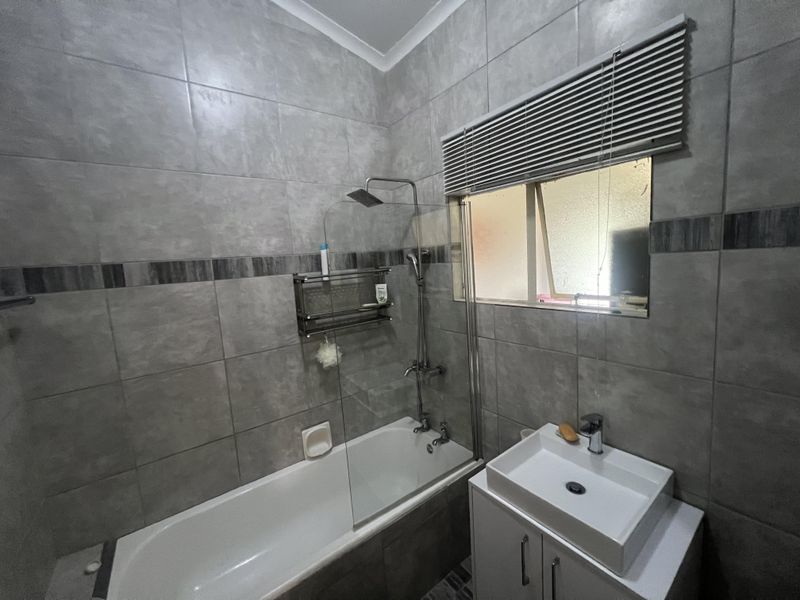 Modern bathroom featuring grey wall tiles, a built-in bathtub with a glass shower screen, rainfall showerhead, and a contemporary vanity basin.