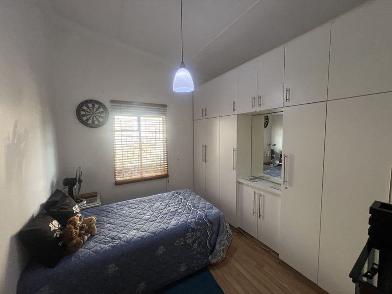 A well-maintained bedroom featuring extensive built-in floor-to-ceiling cabinetry with integrated vanity and mirror, complemented by wood-look flooring and a window with blinds.