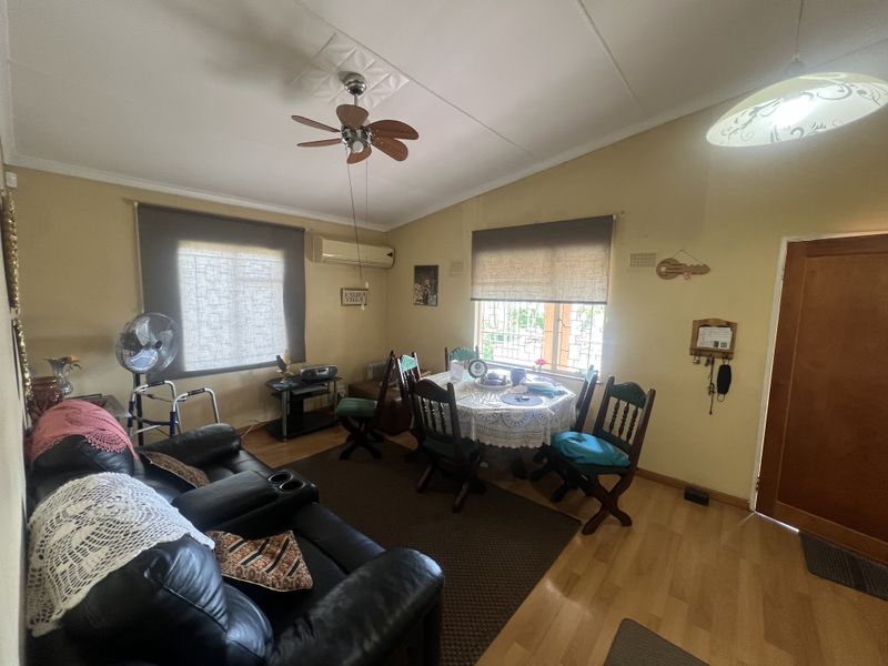 A combined living and dining area featuring a ceiling fan, wall-mounted air conditioning unit, and laminate flooring.