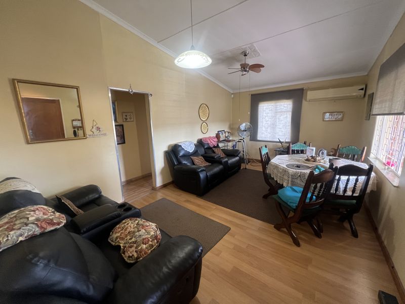 Open plan living and dining area featuring laminate flooring, a ceiling fan, and a wall-mounted air conditioning unit.