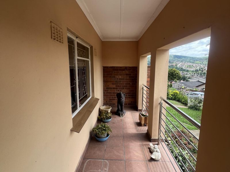 A covered balcony featuring tiled flooring, brick accent wall, and stainless steel railings, offering elevated views of the surrounding neighborhood.