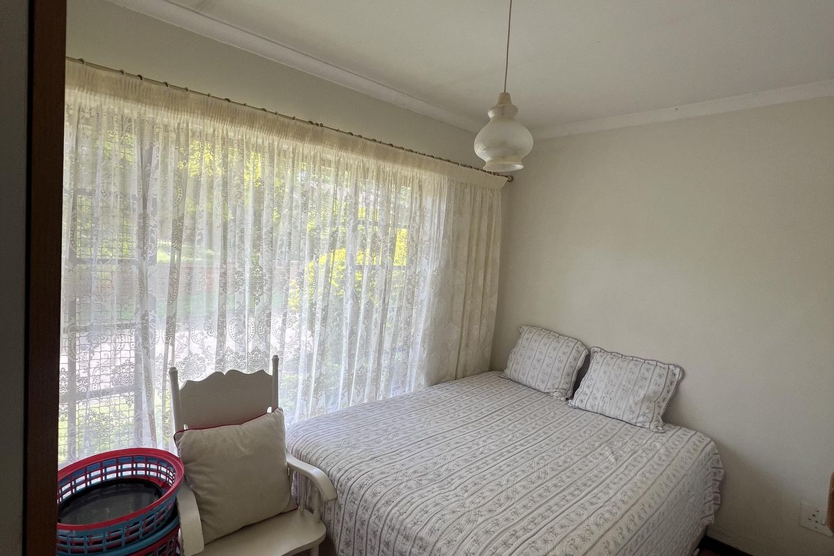 A compact bedroom featuring tiled flooring, a large window with natural light, and a central pendant light fixture.
