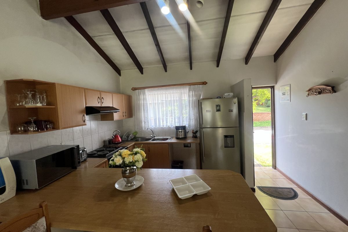 A functional kitchen featuring wooden cabinetry, exposed ceiling beams, and a breakfast bar, with direct access to the exterior.