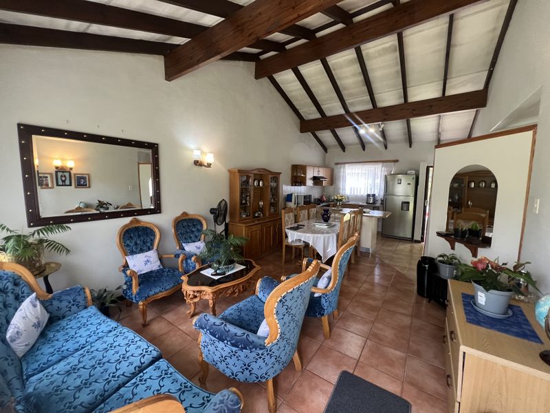 Open-plan living and dining area featuring vaulted ceilings with exposed timber beams and terracotta-style floor tiles, flowing into a functional kitchen space.