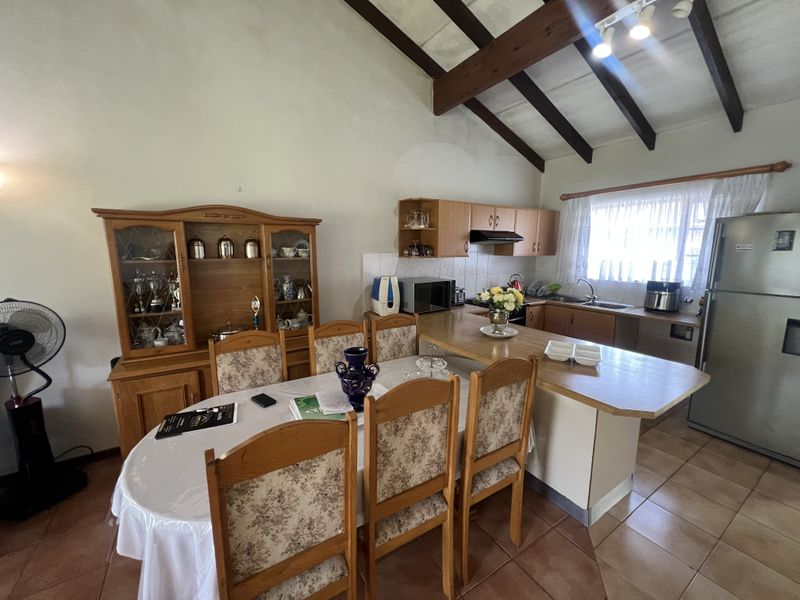 Open-plan kitchen and dining area featuring vaulted ceilings with exposed timber beams, wooden cabinetry, and a breakfast bar counter.